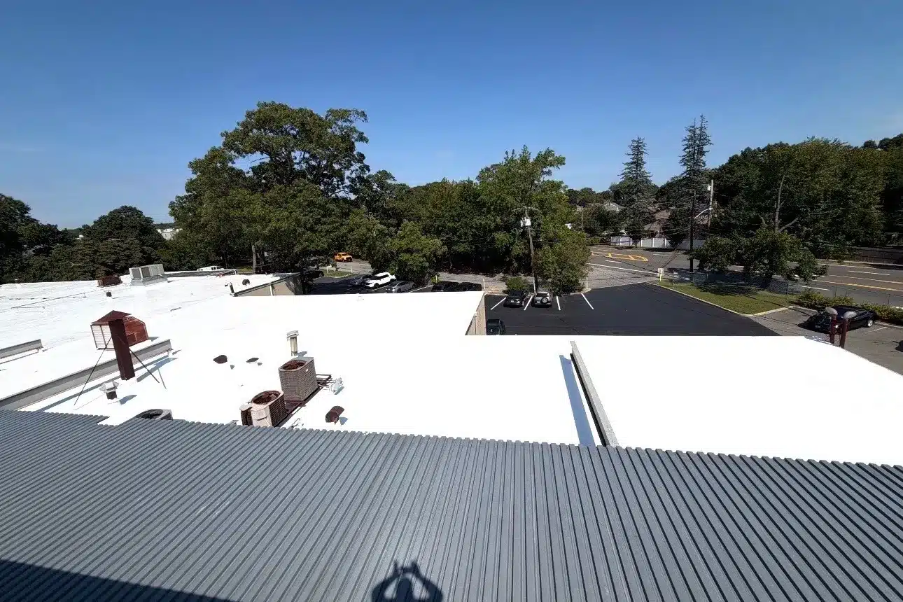 White-coated commercial flat roof with rooftop HVAC units and an adjacent metal roof in Westbury, NY